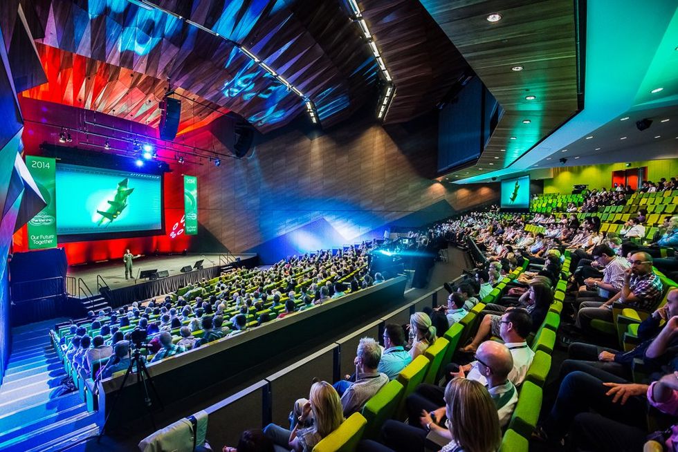 Large audience in modern auditorium watching speaker on brightly lit conference stage