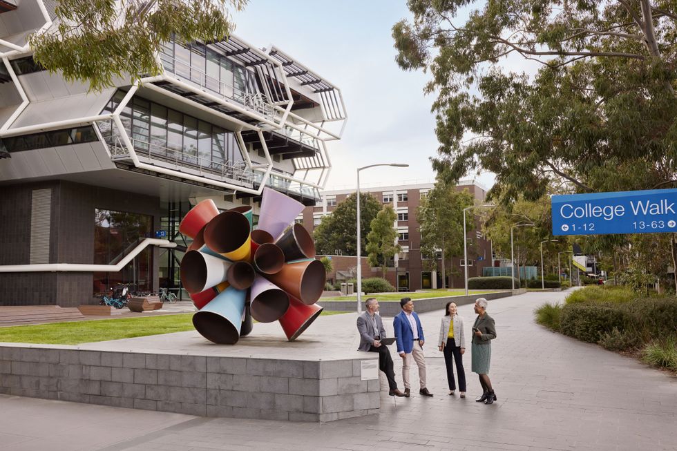 People talking beside colorful cone sculpture outside modern campus building on College Walk