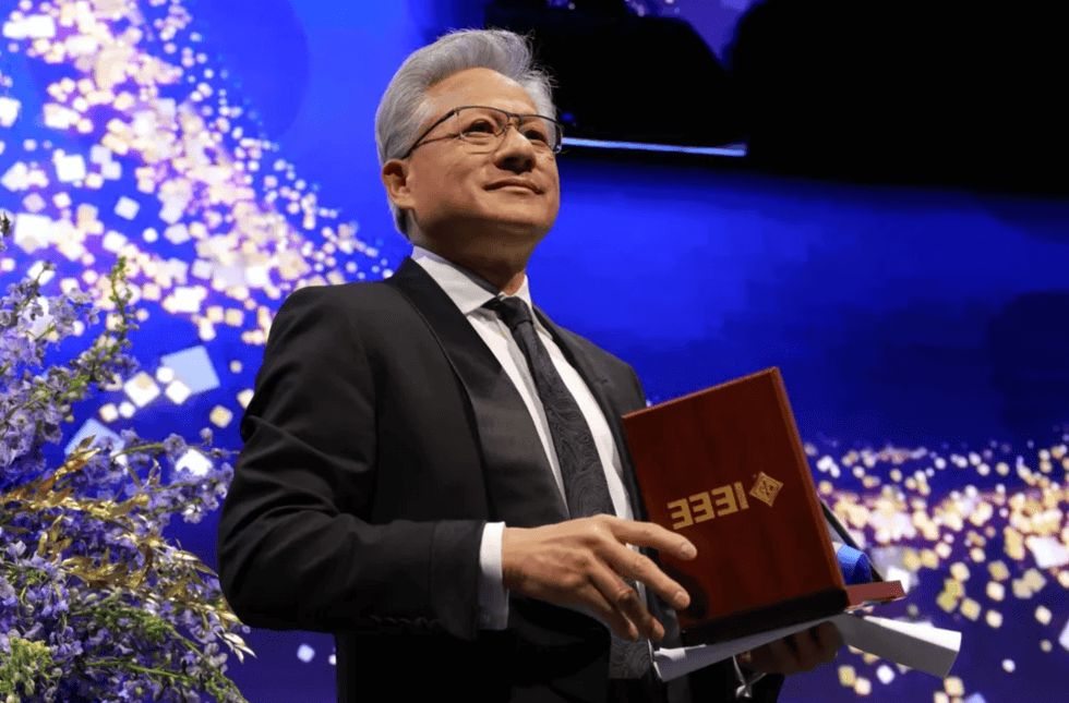 Person in tuxedo holding an IEEE award plaque on a lit stage with floral decor