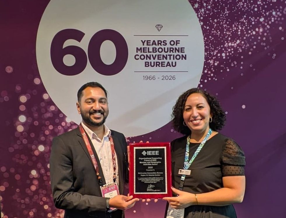 Two people hold an IEEE award in front of a 60 years Melbourne Convention banner