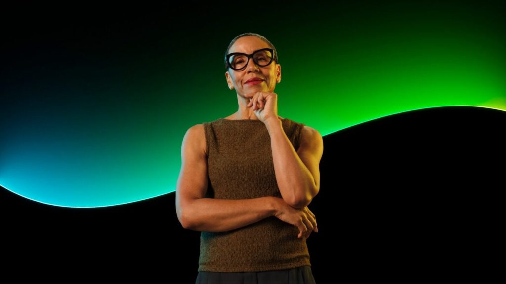A woman poses in front of the Sage glow line and a black background.