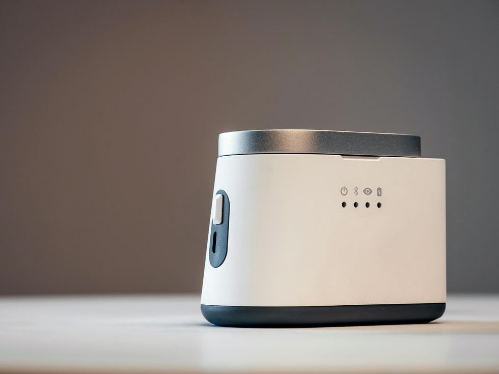 A small obround device with a simple design featuring one button, a lid and four small indicator lights.
