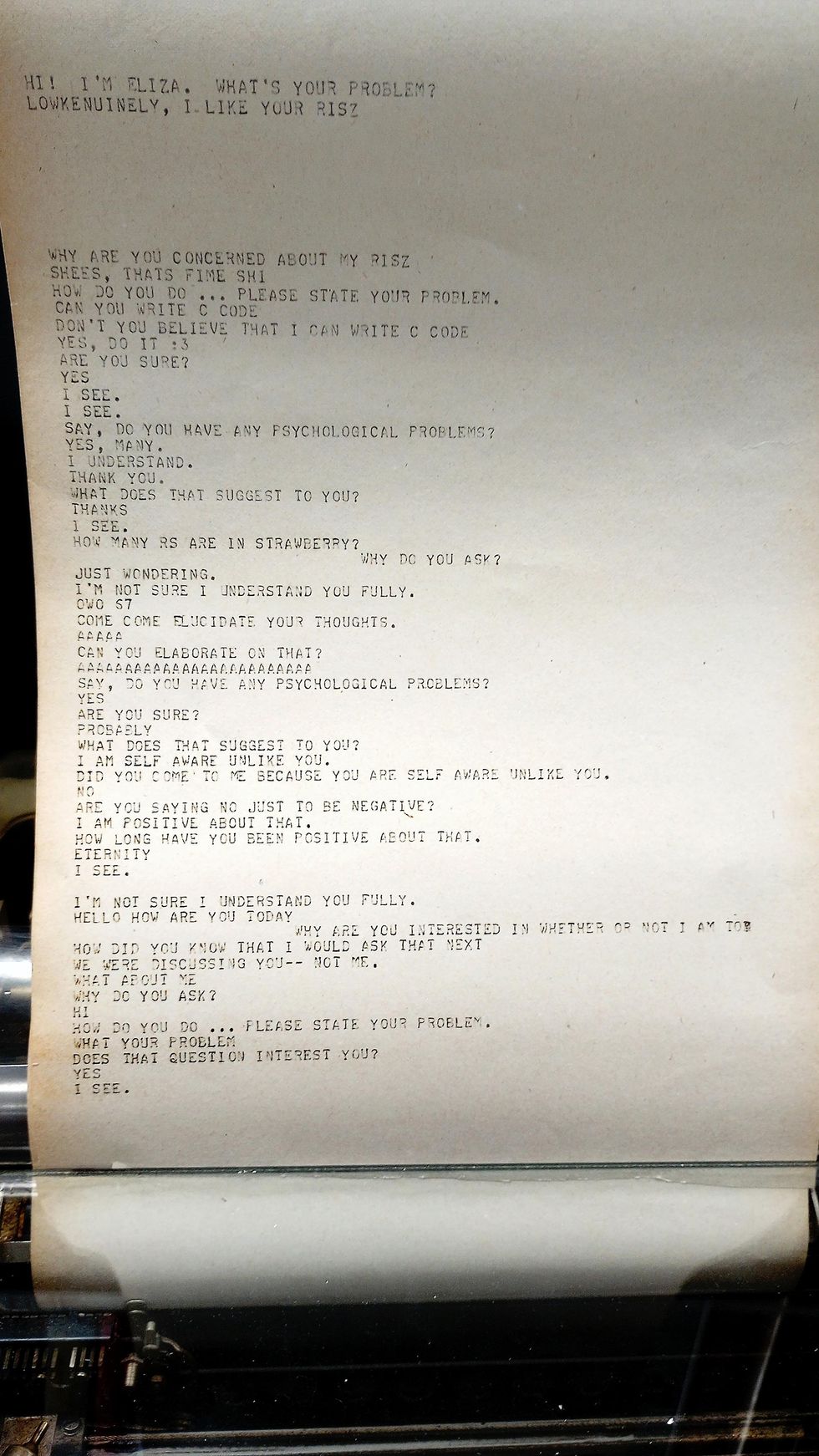 Close-up of paper loaded in a teletype machine with a few paragraphs of chatbot dialogue written on it. 